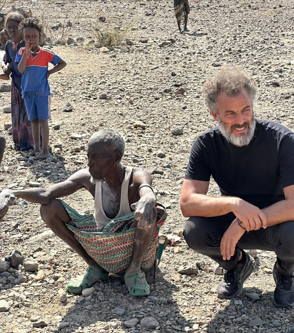 Boubker Benjelloun crouched beside an elderly resident during a field visit, Mandera County